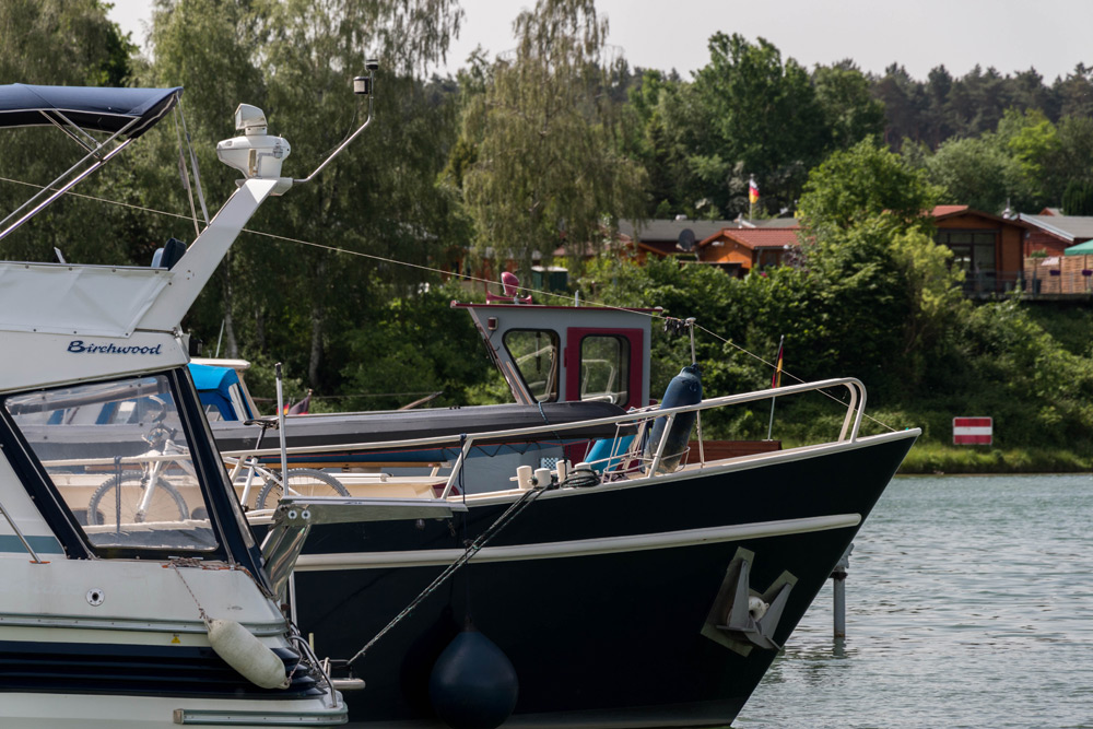 Zwei Motorboote liegen Seite an Seite an einem Fluss mit Bäumen und Hütten im Hintergrund.