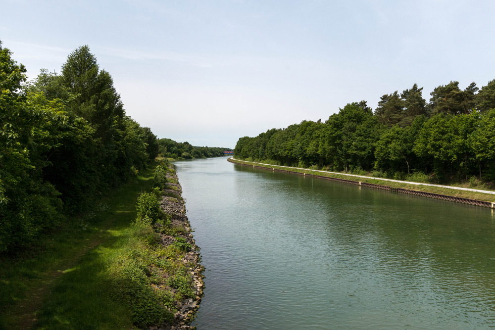 Ein ruhiger Kanal, gesäumt von dichten grünen Bäumen und grasbewachsenen Ufern unter einem klaren Himmel.
