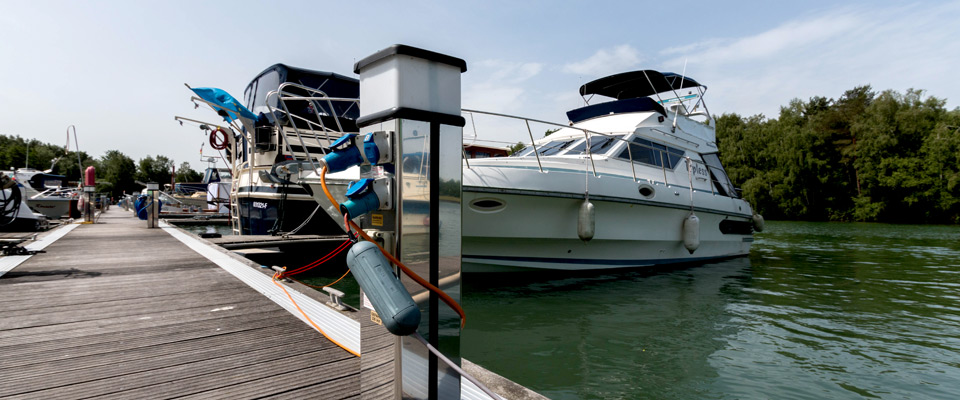 Eine weiße Motoryacht, die in einem Yachthafen liegt, mit einem Elektrizitätswerk im Vordergrund und Bäumen im Hintergrund.
