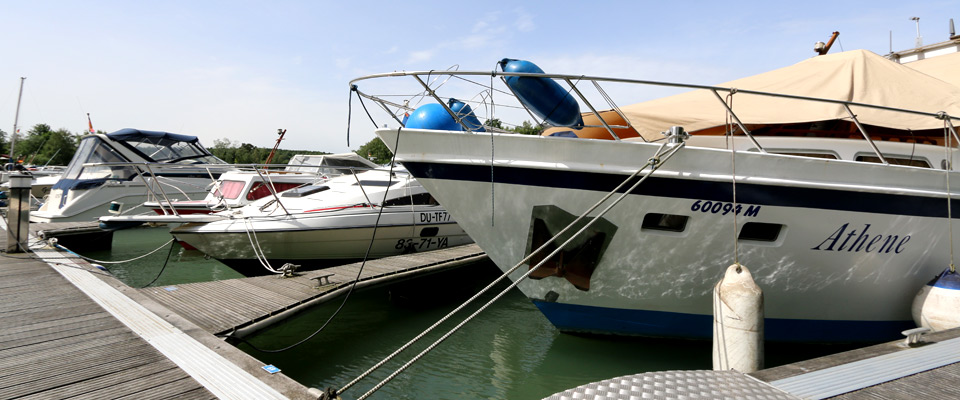 Mehrere Motorboote und Yachten, darunter eine mit dem Namen Athene, liegen an einem sonnigen Tag an einem hölzernen Hafenpier.